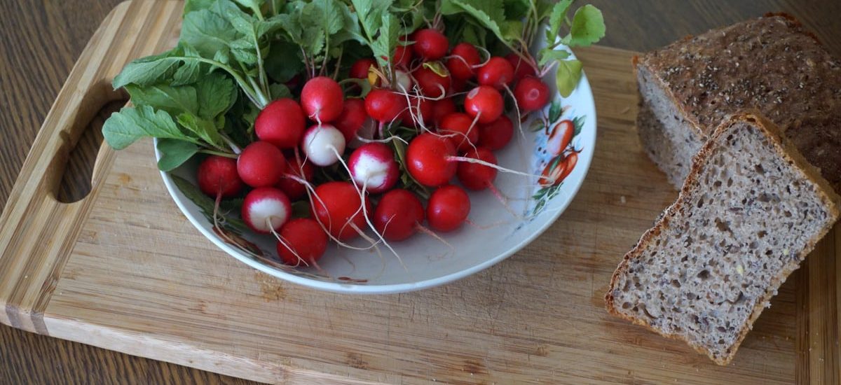 A vibrant display of radishes with leafy greens and whole grain bread on a wooden cutting board.