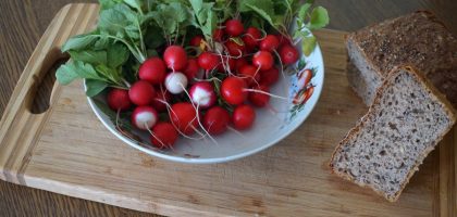 A vibrant display of radishes with leafy greens and whole grain bread on a wooden cutting board.