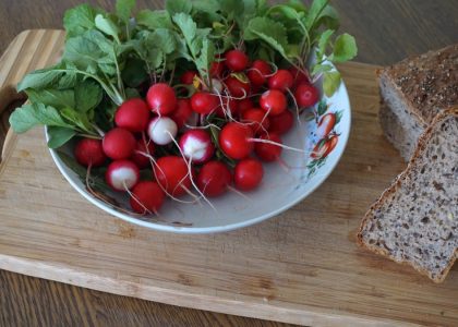 A vibrant display of radishes with leafy greens and whole grain bread on a wooden cutting board.